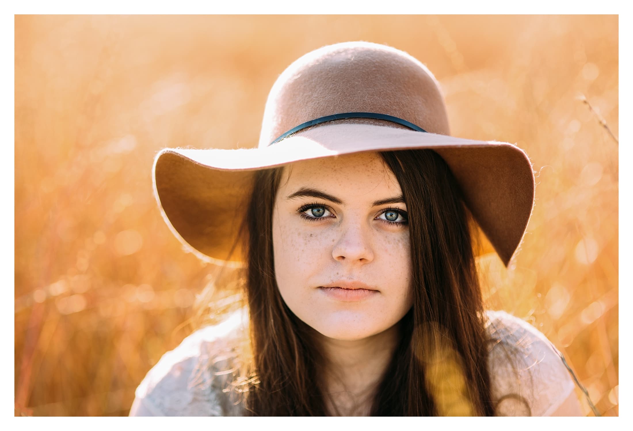 Teenage daughter sitting in field with a brown floppy hat.
