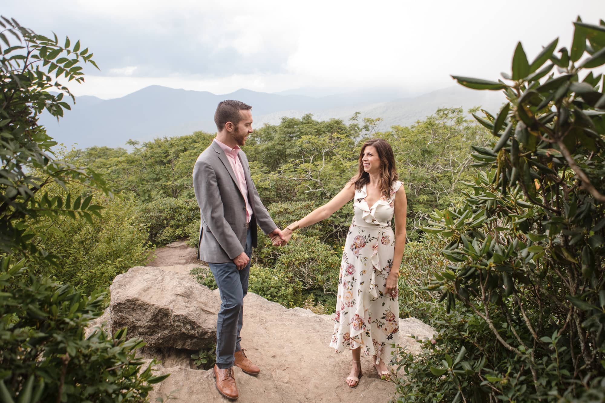 Couple holding hands on rock with mountain backdrop near Asheville North Carolina photography done by Kathy Beaver.
