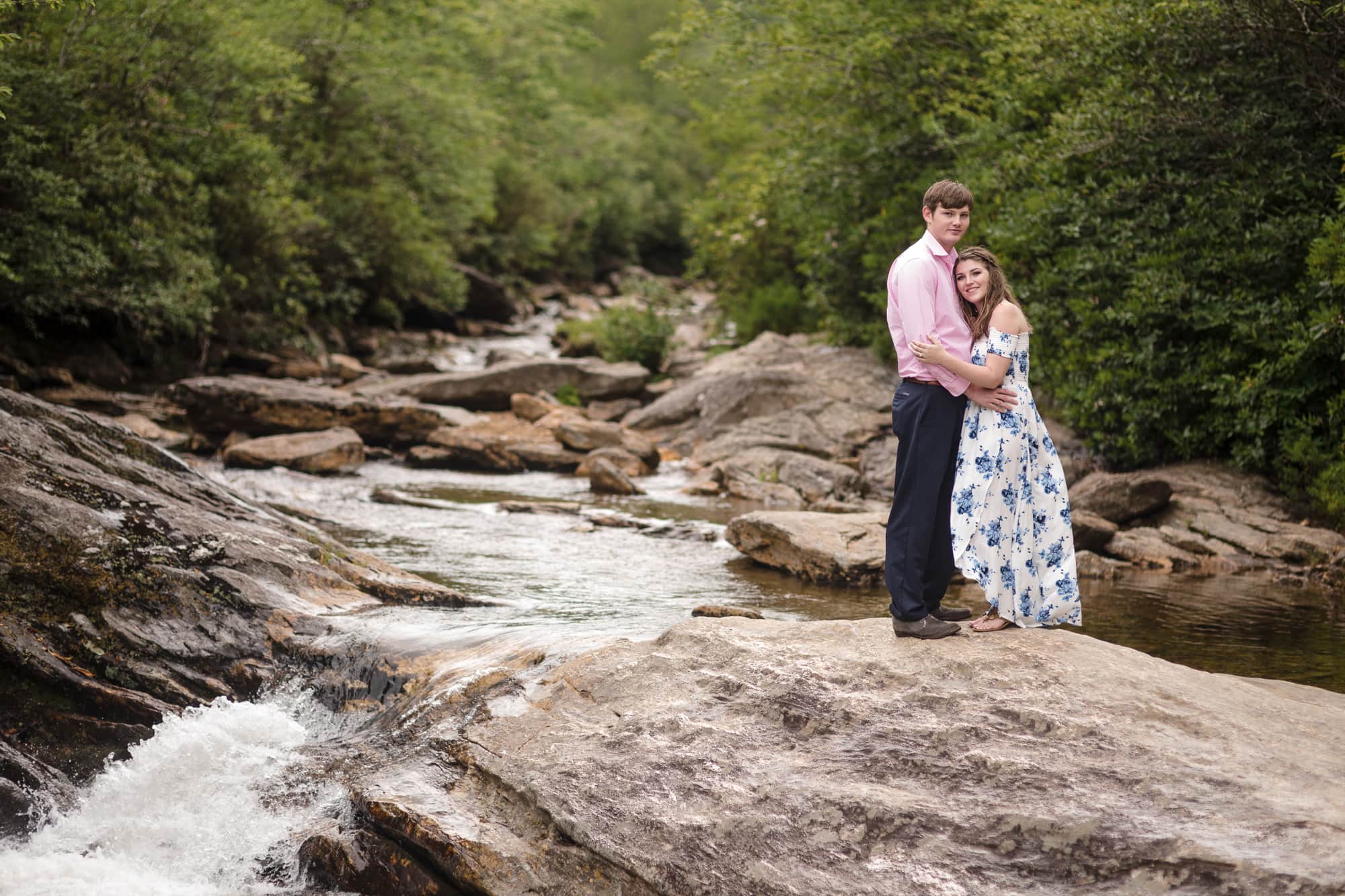 Couple hugging on rock near river in Brevard North Carolina photography done by Kathy Beaver.