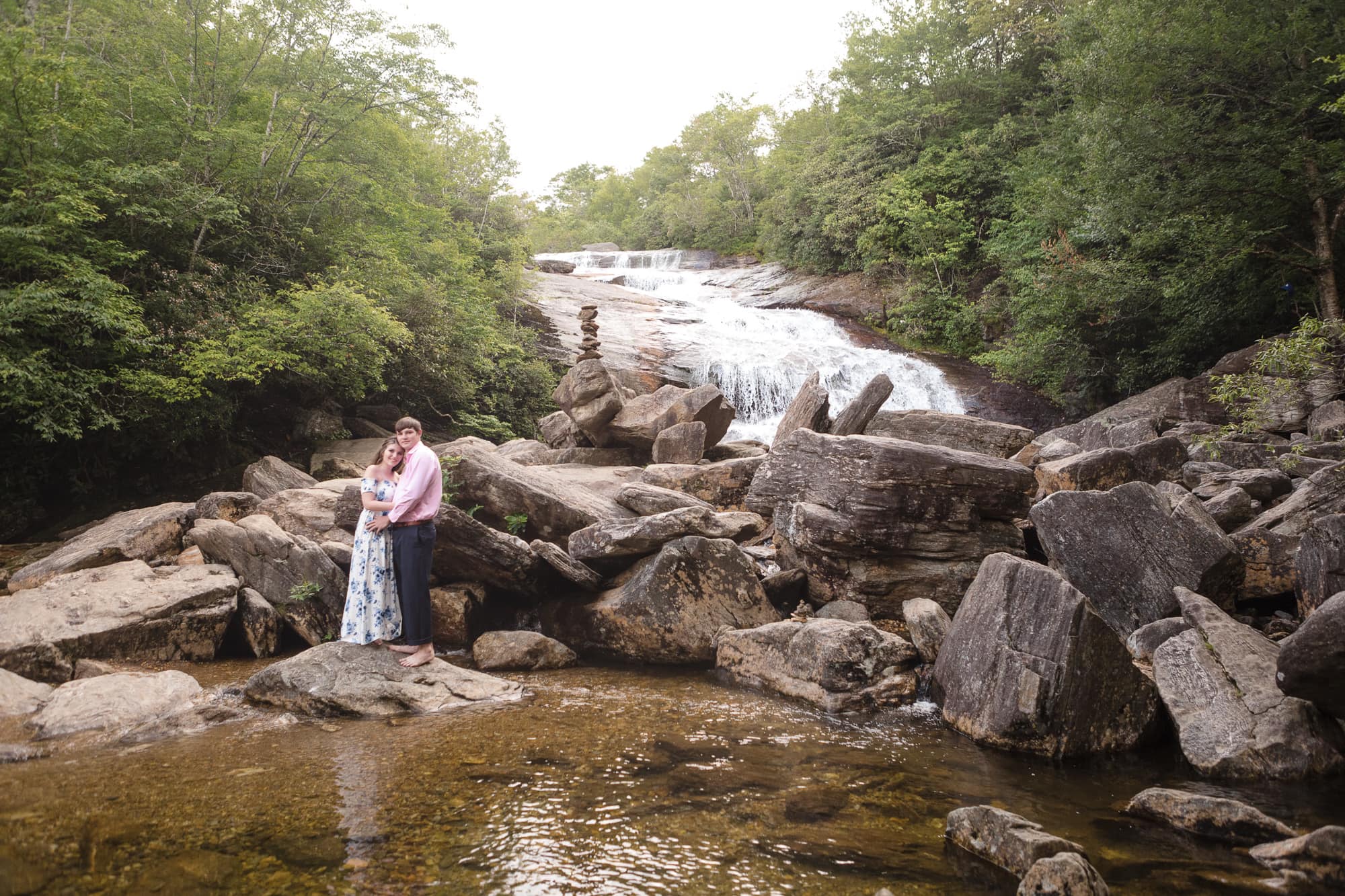 Couple standing on rock near with waterfall behind them in Brevard North Carolina photography done by Kathy Beaver.