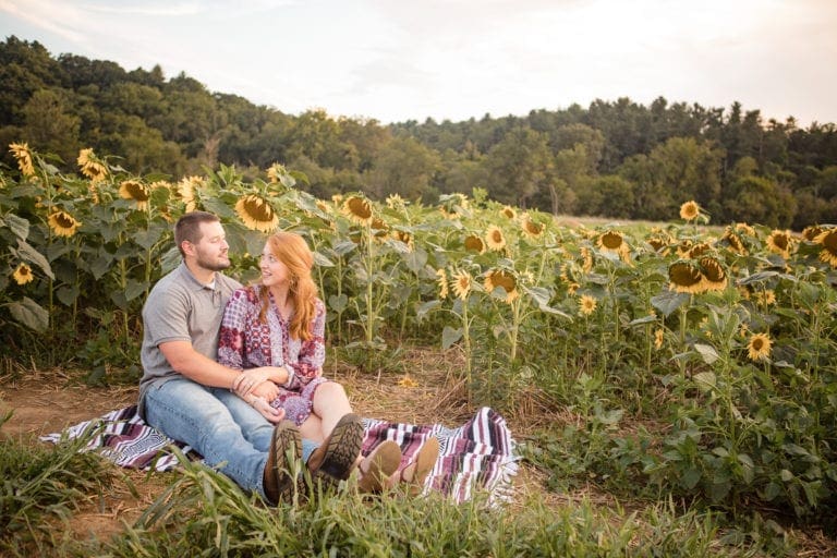 Couple sitting in sunflower field holding hands at Biltmore Estate North Carolina photography done by Kathy Beaver.