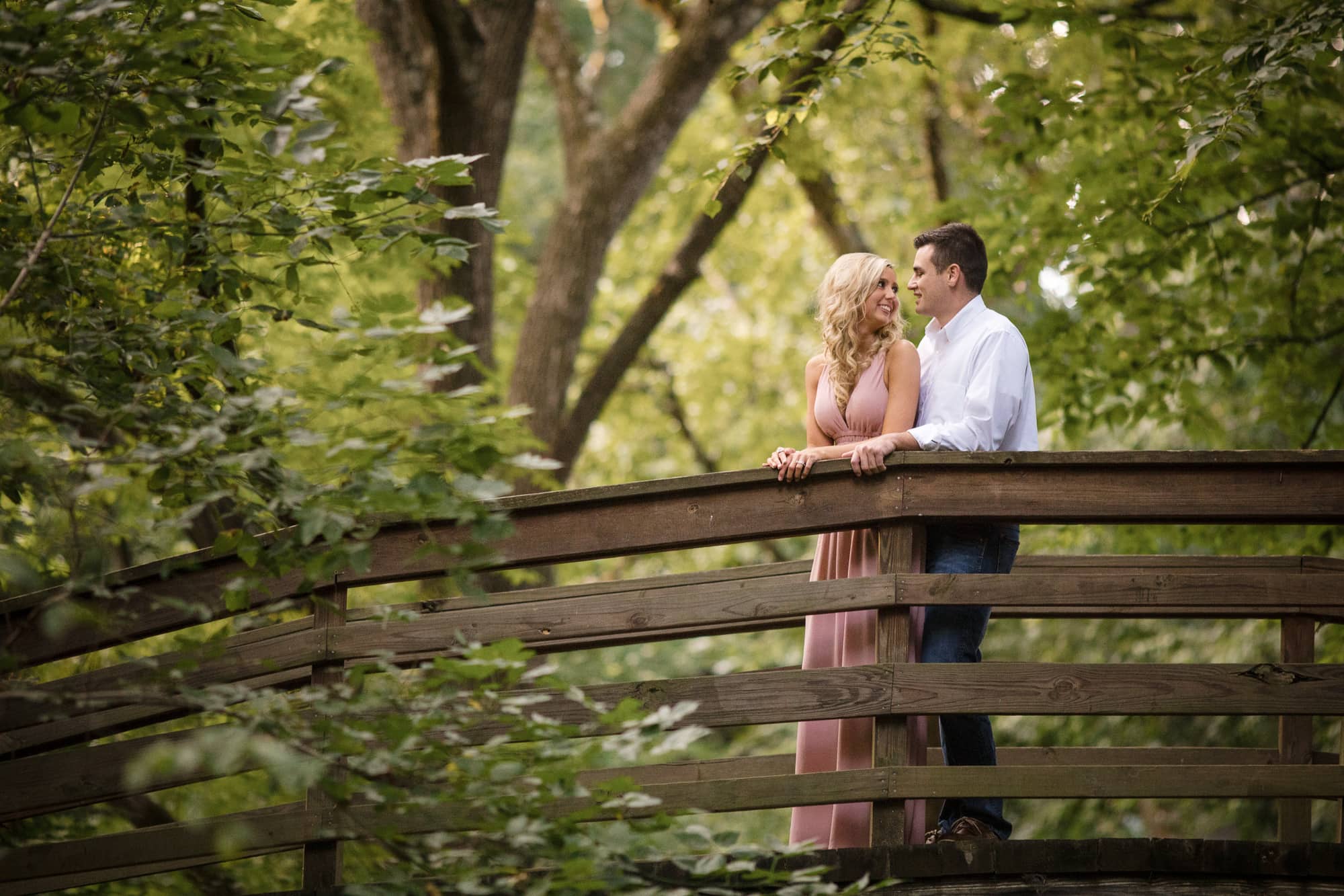 Couple smiling at one another standing on bridge in wooded park in Asheville, North Carolina photography done by Kathy Beaver.