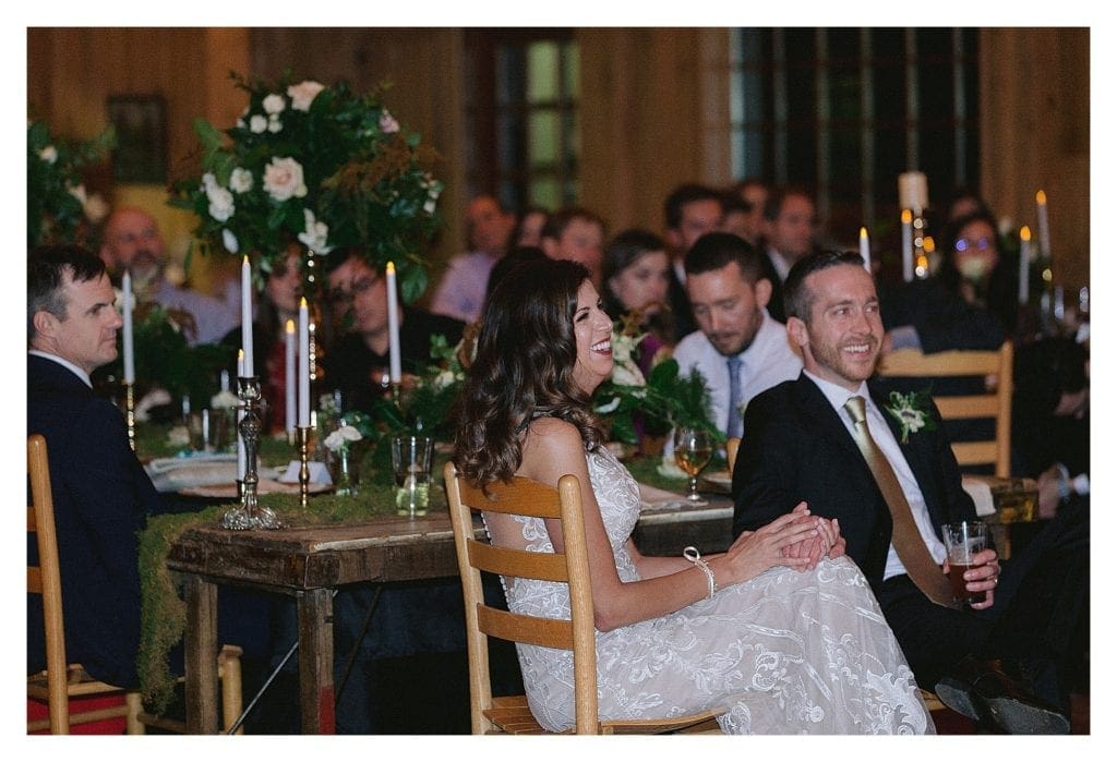 Bride and groom laughing while sitting holding hands and listening to wedding speeches - kathy beaver photography