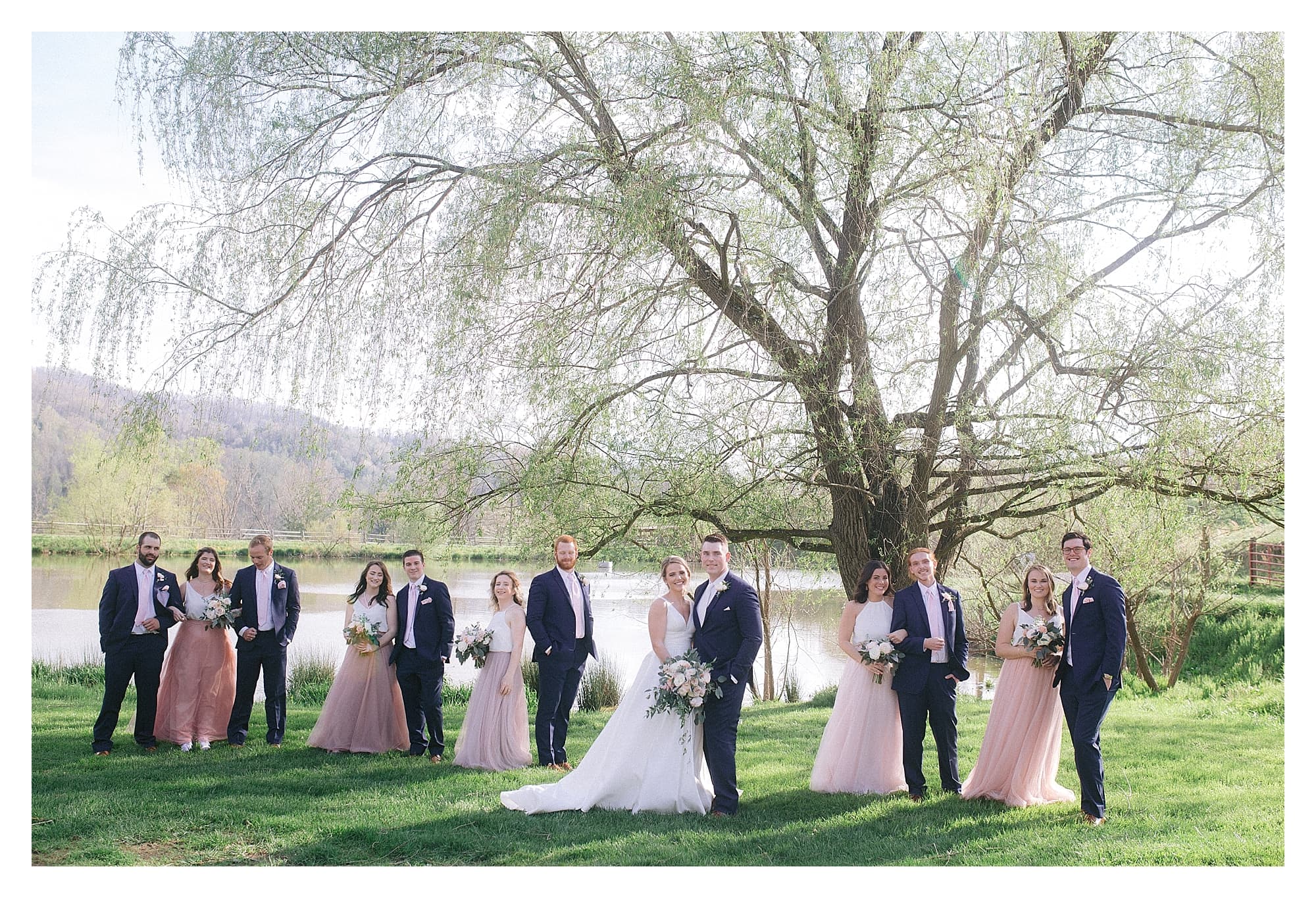 Wedding party posing beside pond under willow tree