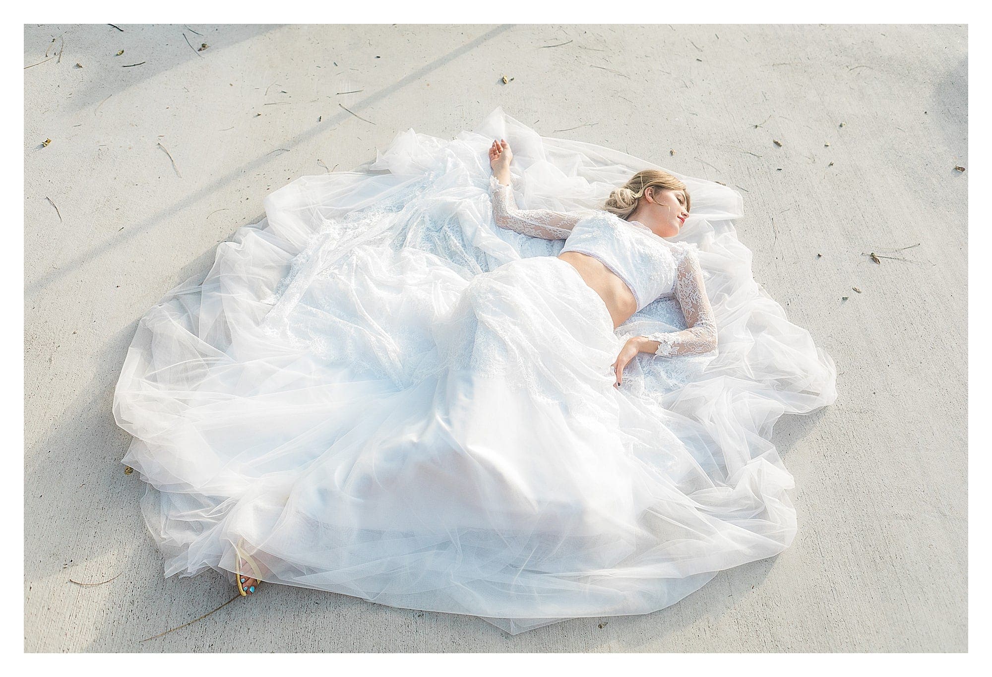 Bride wearing two piece white lace wedding dress laying on concrete posing