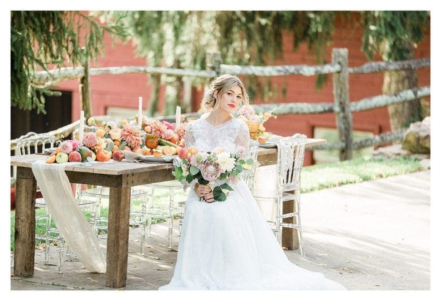 Bride wearing two piece white lace wedding dress holding peach, pink and yellow themed wedding bouquet