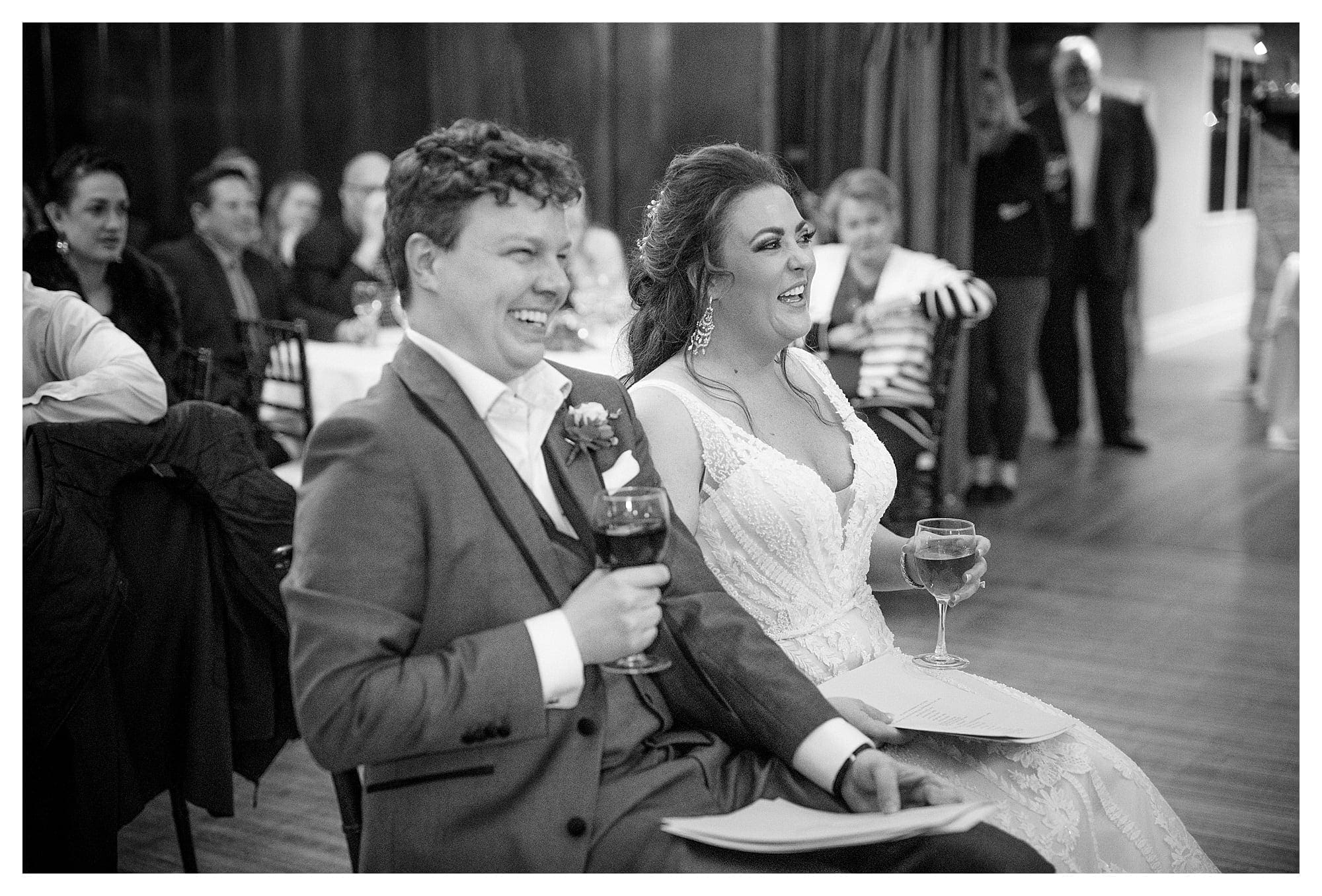 black and white photo of bride and groom laughing during toasts at wedding reception