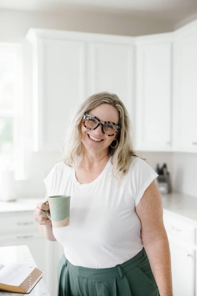 A woman in glasses holding a coffee mug.