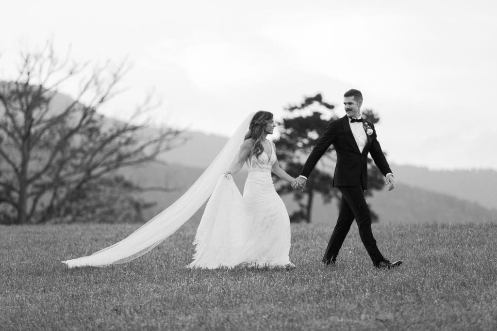 The bride and groom walk holding hands with mountains in the background | Kathy Beaver Photography | Asheville Wedding Photographer