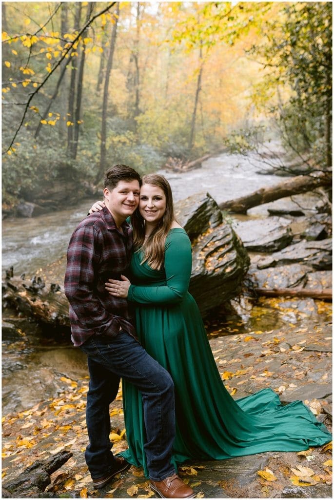 Fall engagement photos by the river in Asheville, wearing a green dress and a plaid shirt.