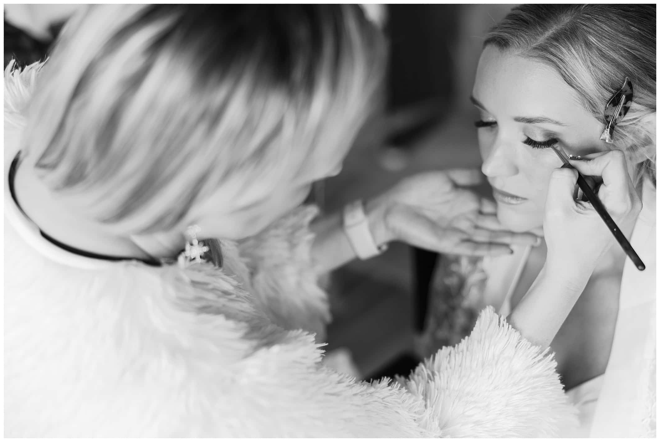 black and white photo of bride getting her makeup done on her wedding day