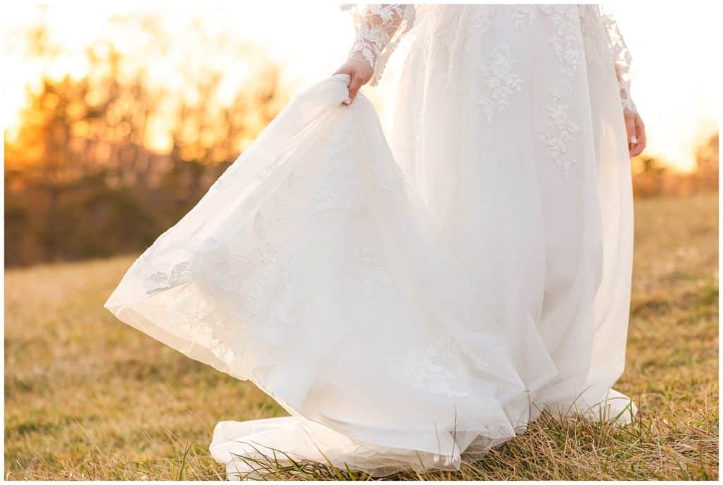 bride holds dress in sunset field