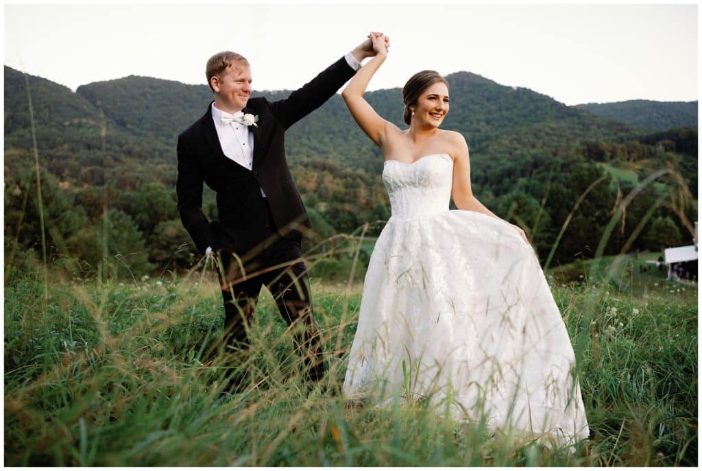 A bride and groom in a field holding hands.