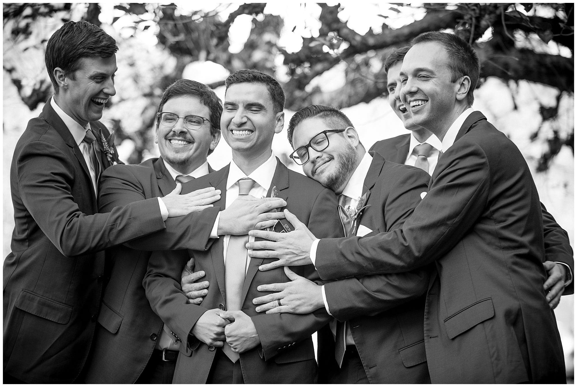 A black and white photo of a group of groomsmen hugging.