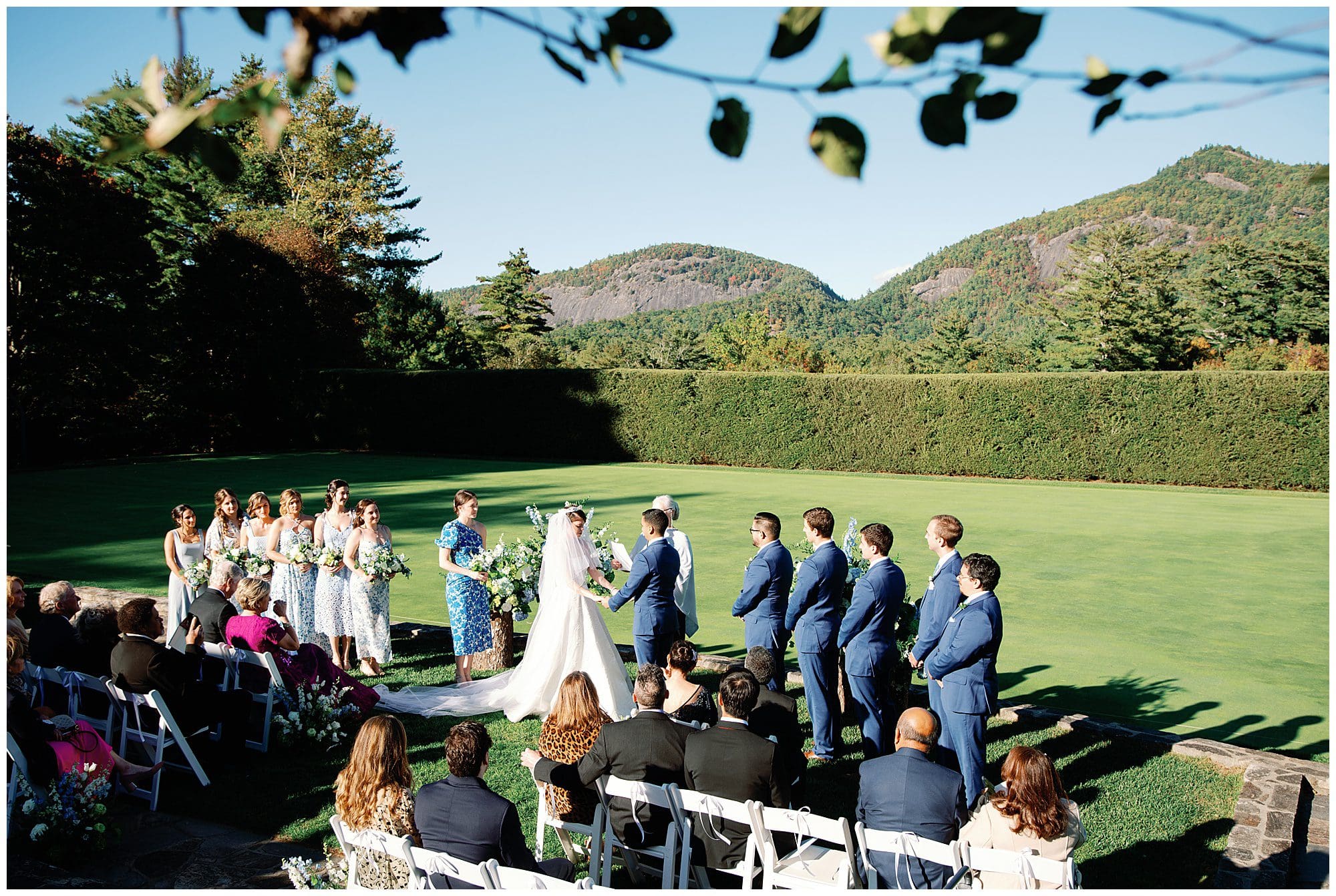A wedding ceremony in a grassy field with mountains in the background.