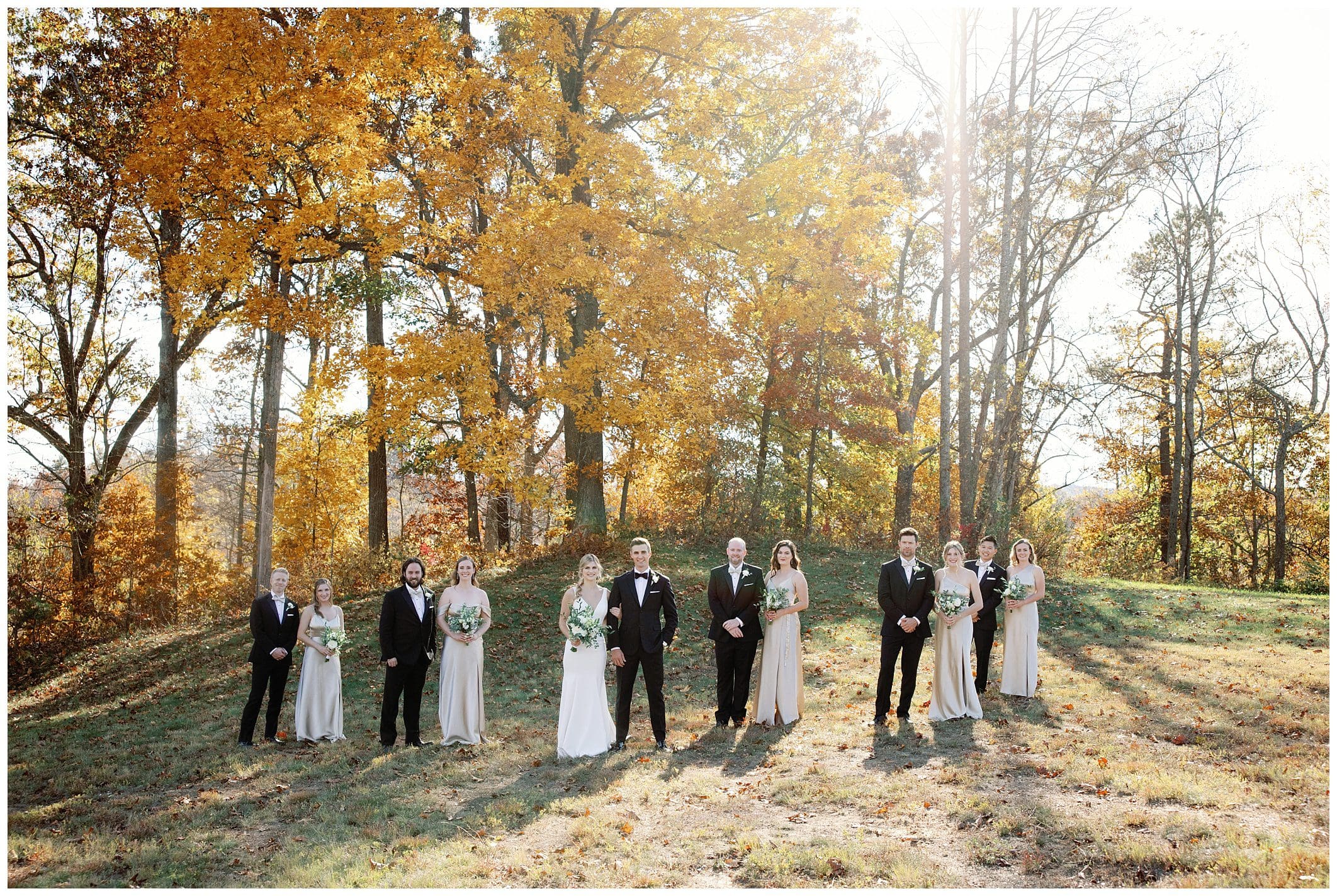 A group of bridesmaids and groomsmen standing in front of trees at a fall wedding at crest center.