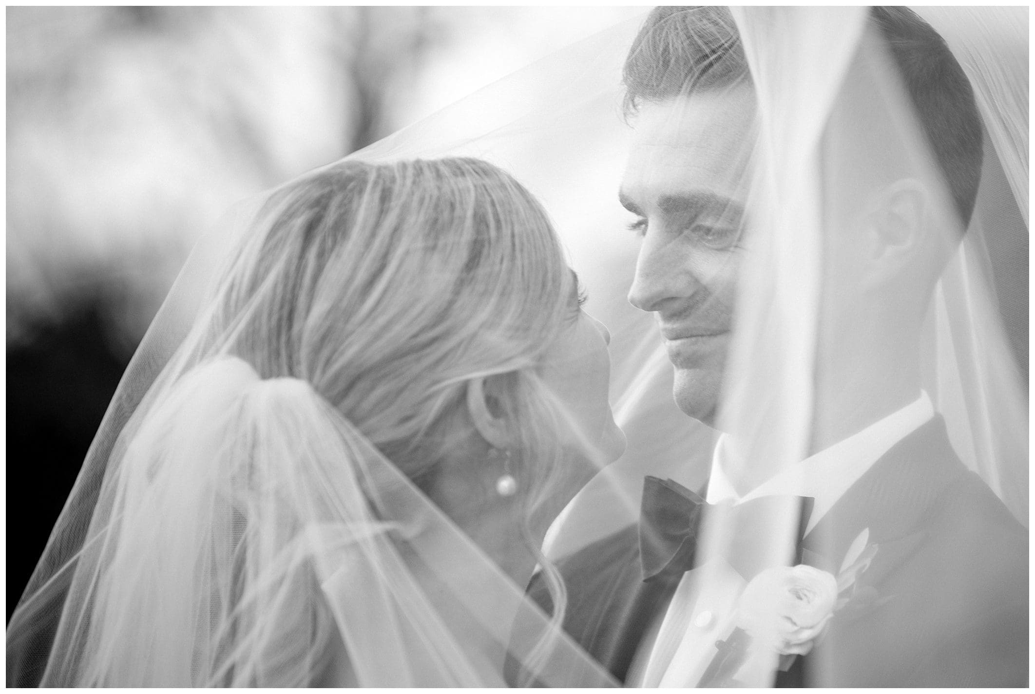 A black and white photo of a bride and groom kissing under a veil at their fall wedding at Crest Center.