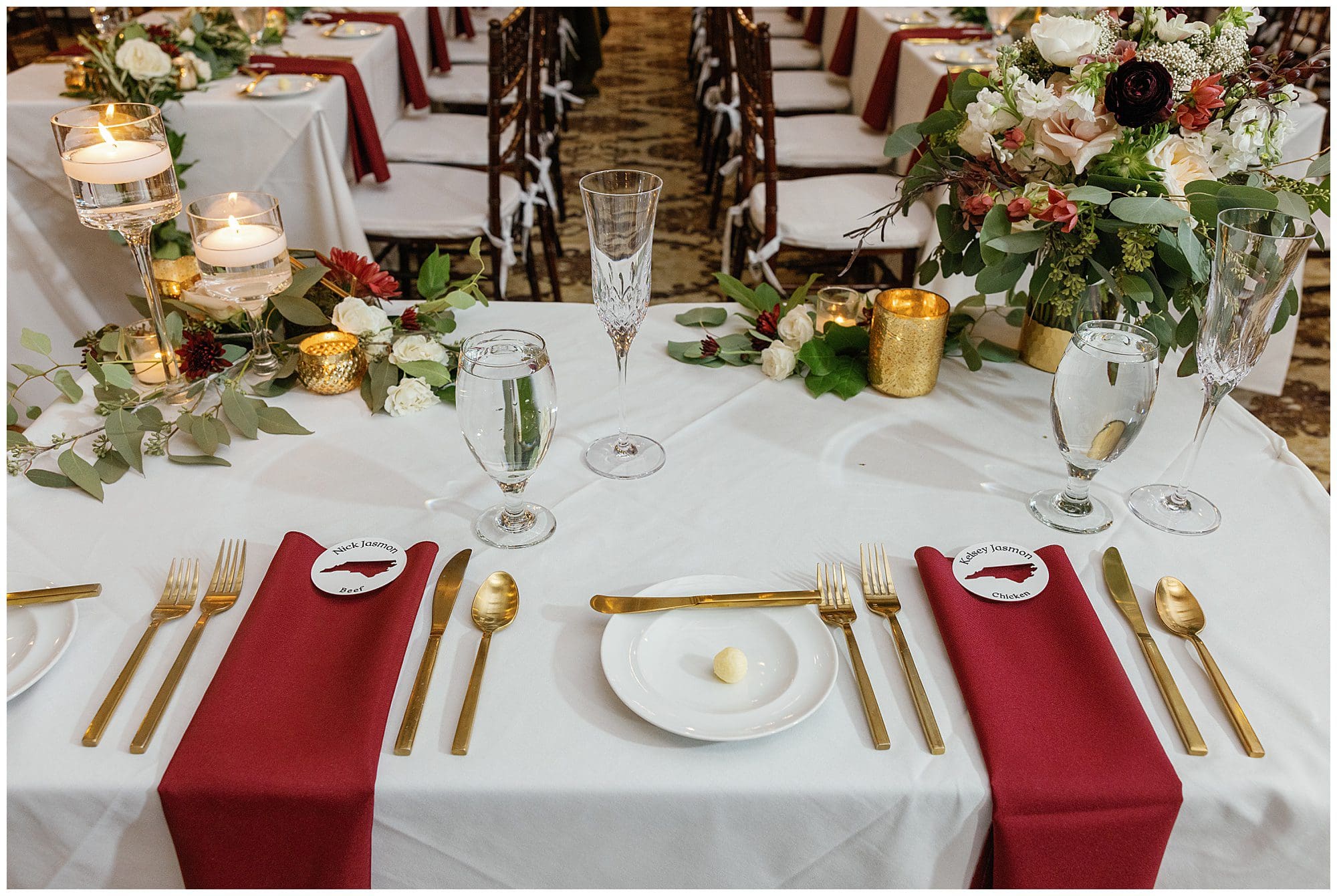 A wedding table setting with gold and burgundy napkins and forks.