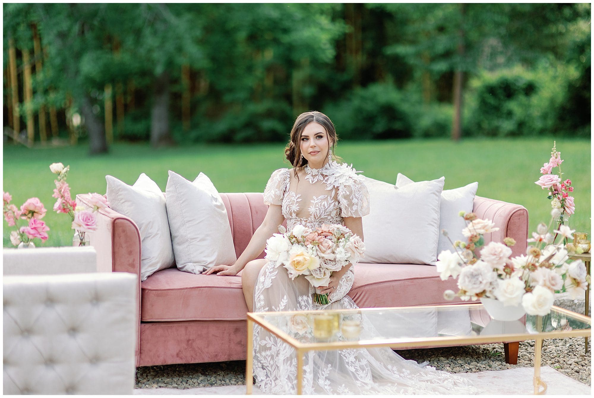 A bride sitting on a pink couch in a garden.