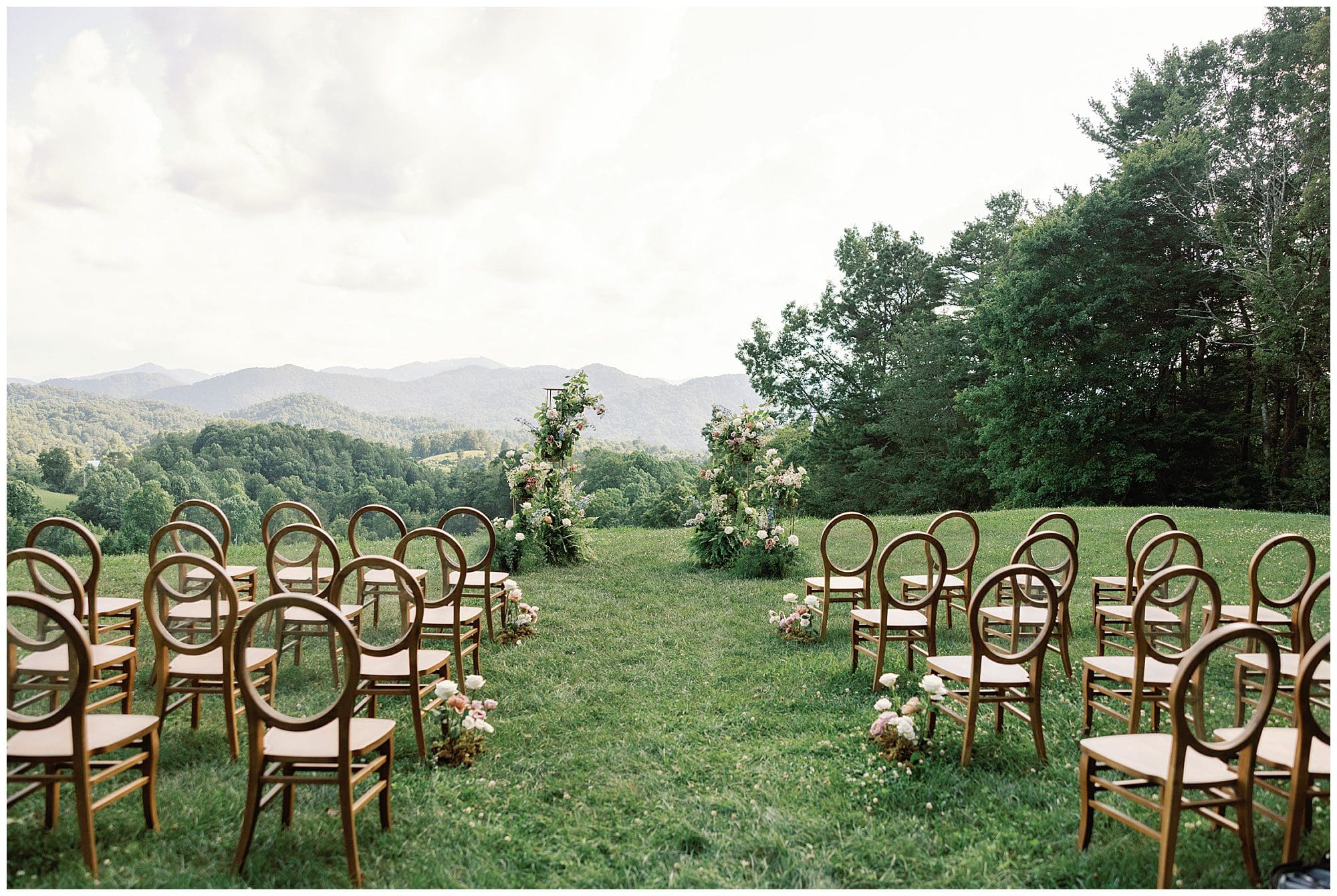 A Parisian-inspired summer wedding ceremony set up in a grassy field with mountains in the background at The Ridge.