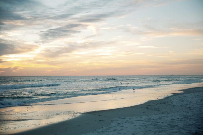 A person is standing on Rosemary Beach at sunset, capturing its beauty through photography during a retreat.