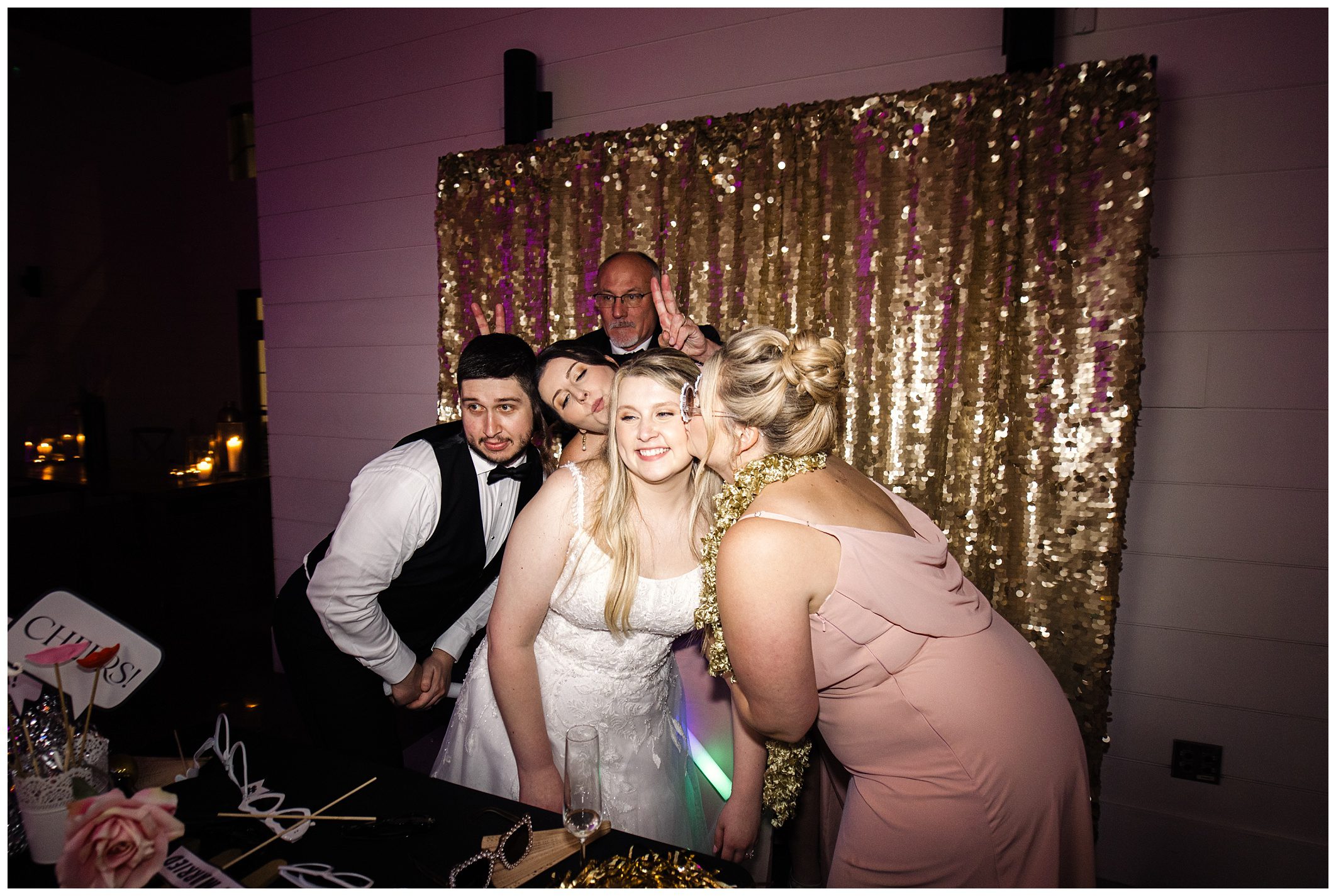 Group of people, including a bride, posing for a photo at a mountain wedding reception with a gold sequin backdrop.