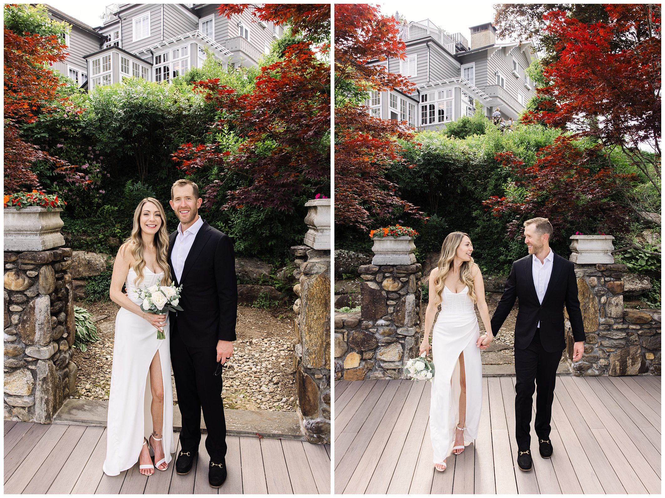 A couple dressed formally stands and walks hand in hand outside a stone building surrounded by greenery and red-leaved trees. The woman wears a white dress, and the man wears a black suit.