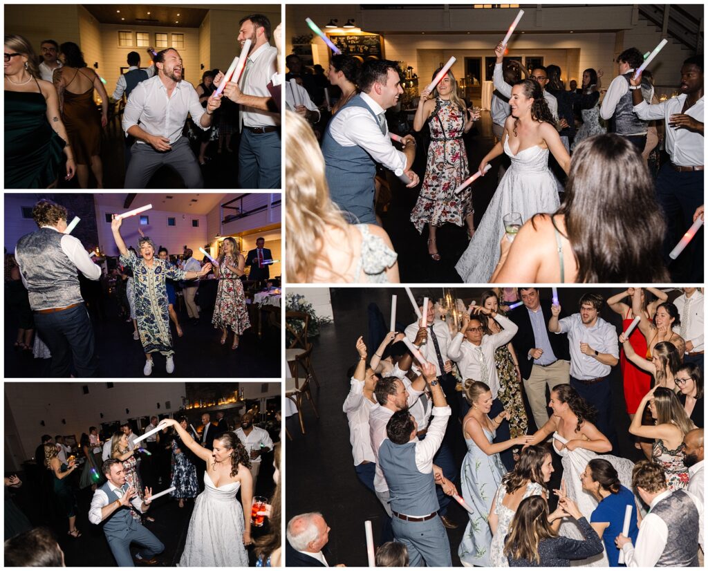 People are dancing and having fun with light sticks at a wedding reception. The bride in a white dress and the groom in a vest are among the group in a lively celebration.