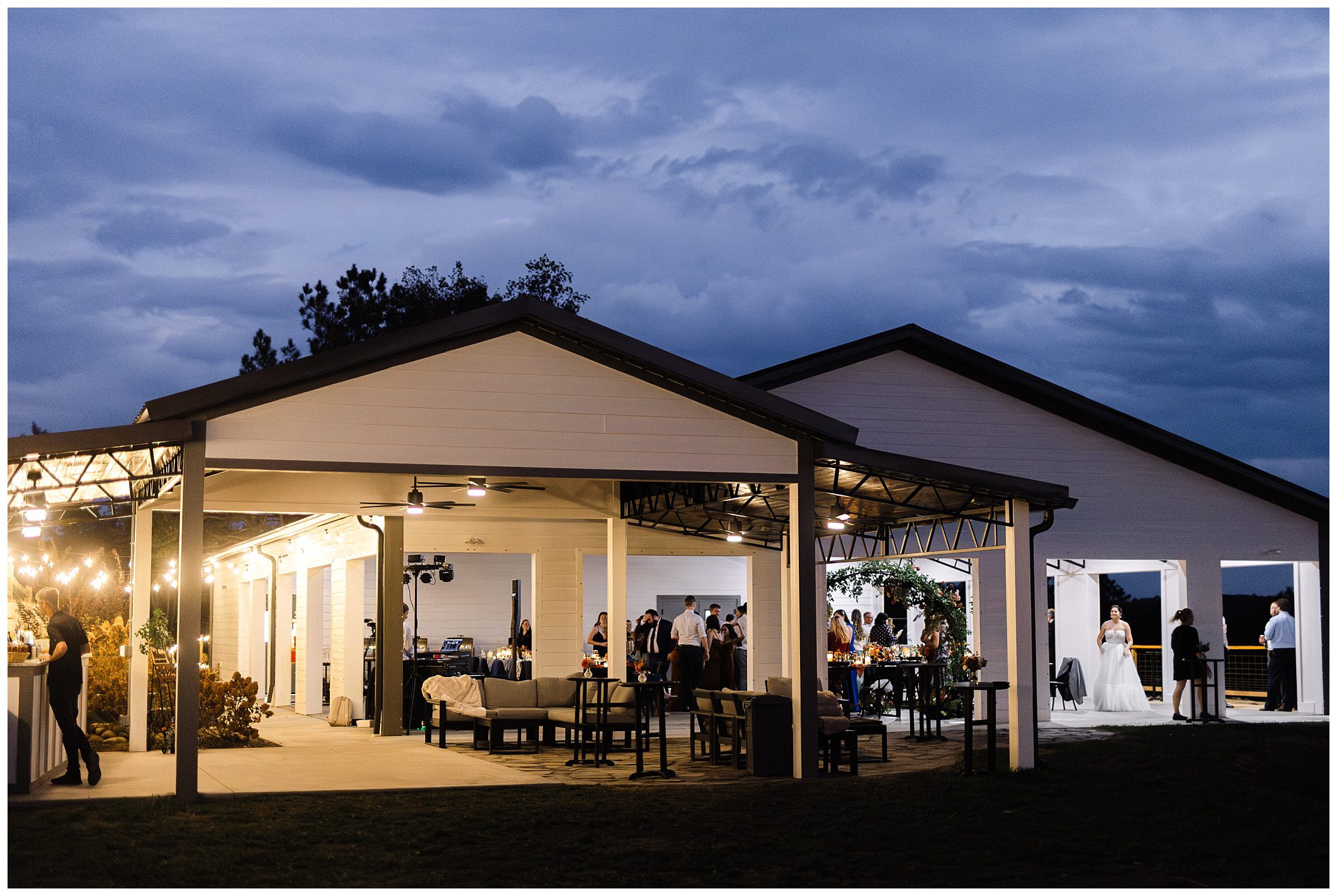 Outdoor evening wedding reception at a lit pavilion, with guests socializing and a couple dancing in the background.