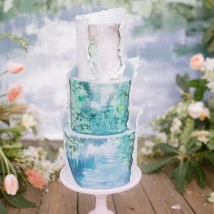 Blue, green and turquoise painted wedding cake wrapped partly with white fondant