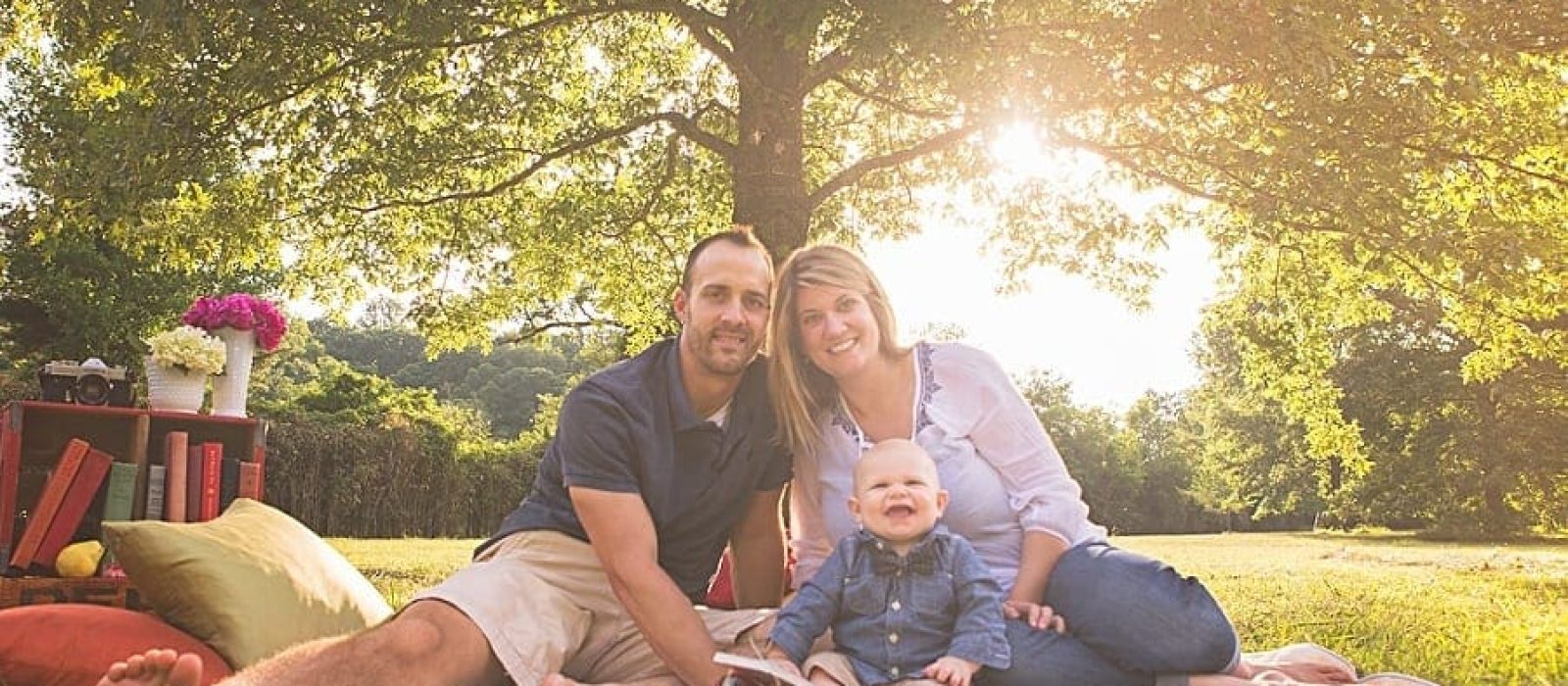 Picnic scene with vintage soda crates and flowers, family sitting on quilt with giggling baby